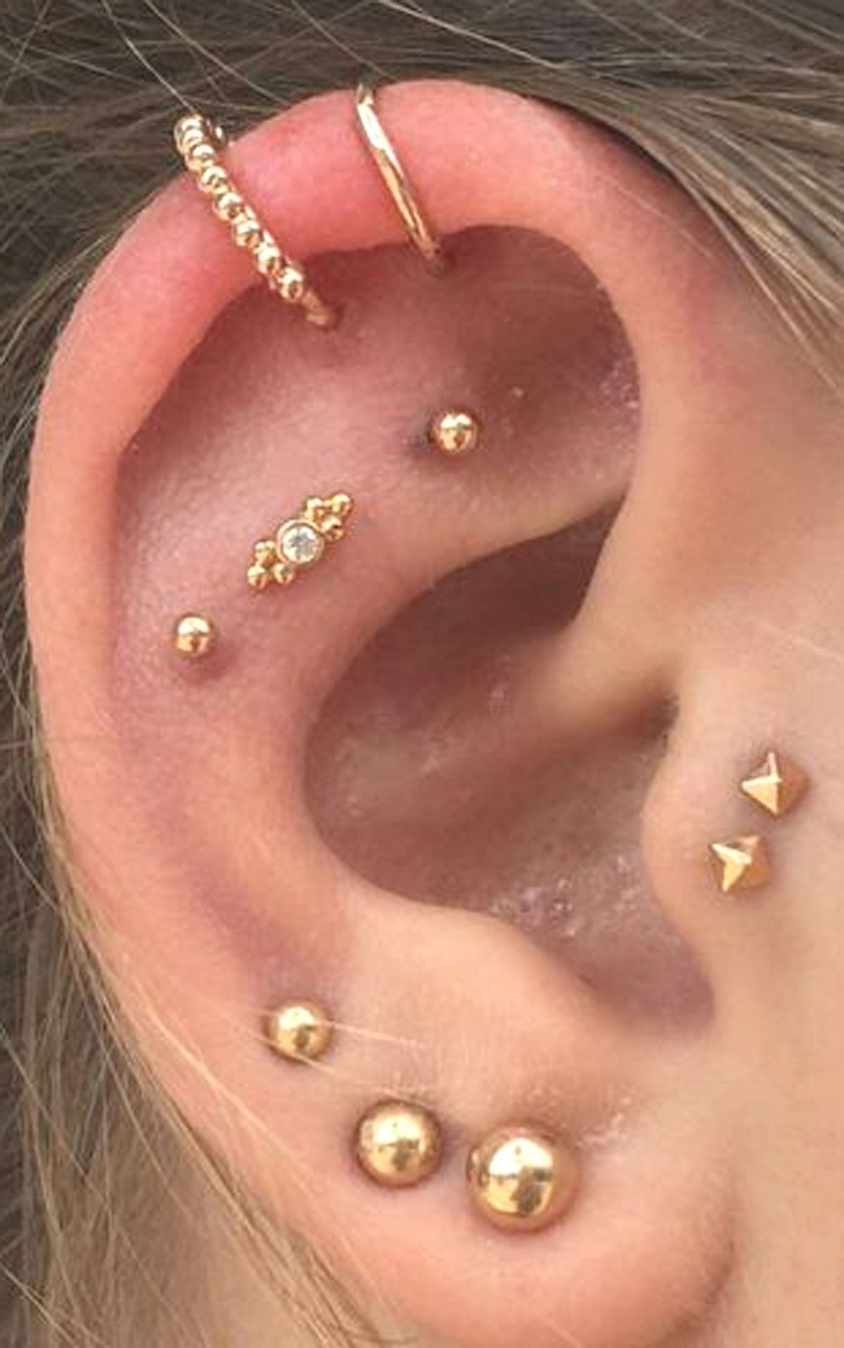 Aplicação de piercing na orelha com joia de ouro cravejada